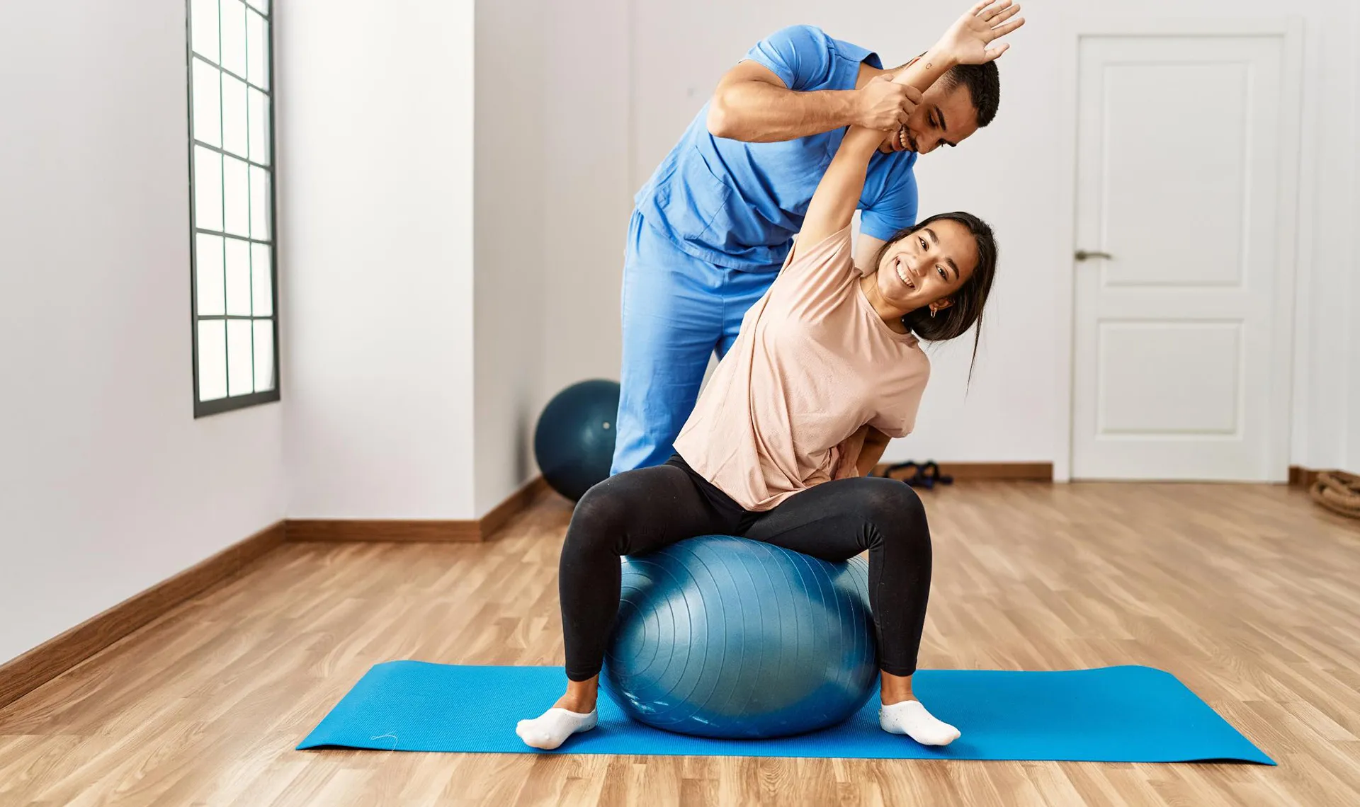 Bewegungstherapie im Reha-Zentrum Weyer – Physiotherapeut unterstützt Patientin bei Dehnübung auf Gymnastikball